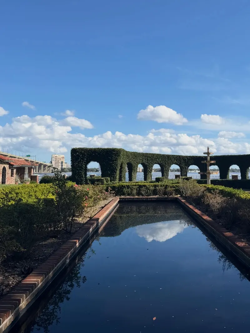A long reflecting pool between clipped hedges under a blue sky