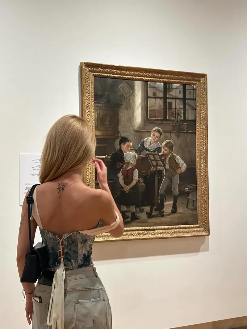 Panh from behind in a laced blue floral corset, facing an old painting in a gallery