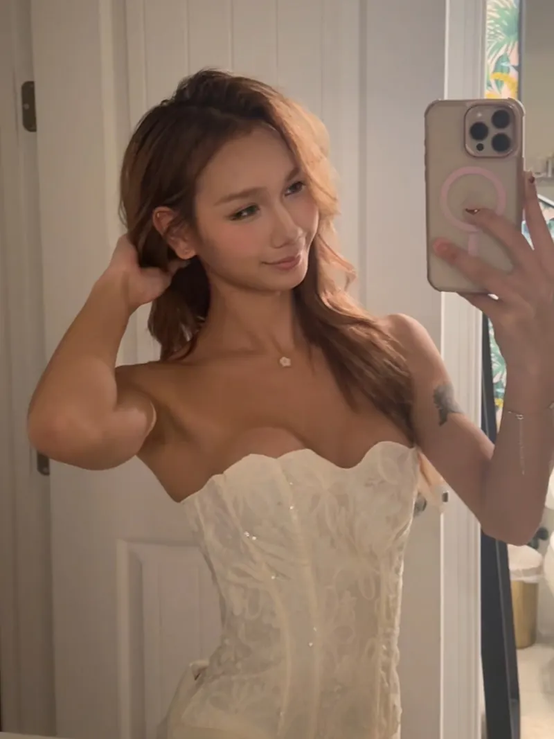 Mirror selfie in a white corset, one arm raised showing a toned bicep