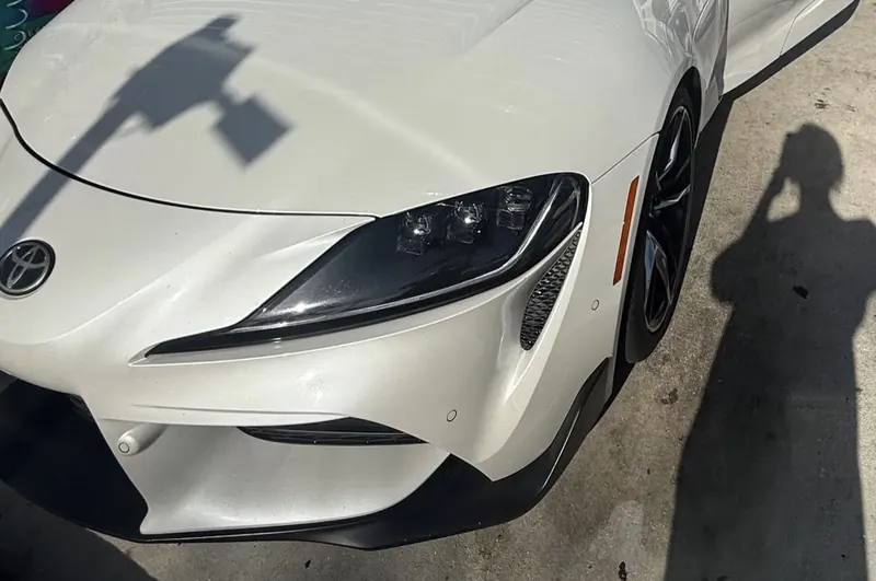 Front of a pearl-white Toyota GR Supra in bright sun, with Panh's shadow on the ground as she takes the photo