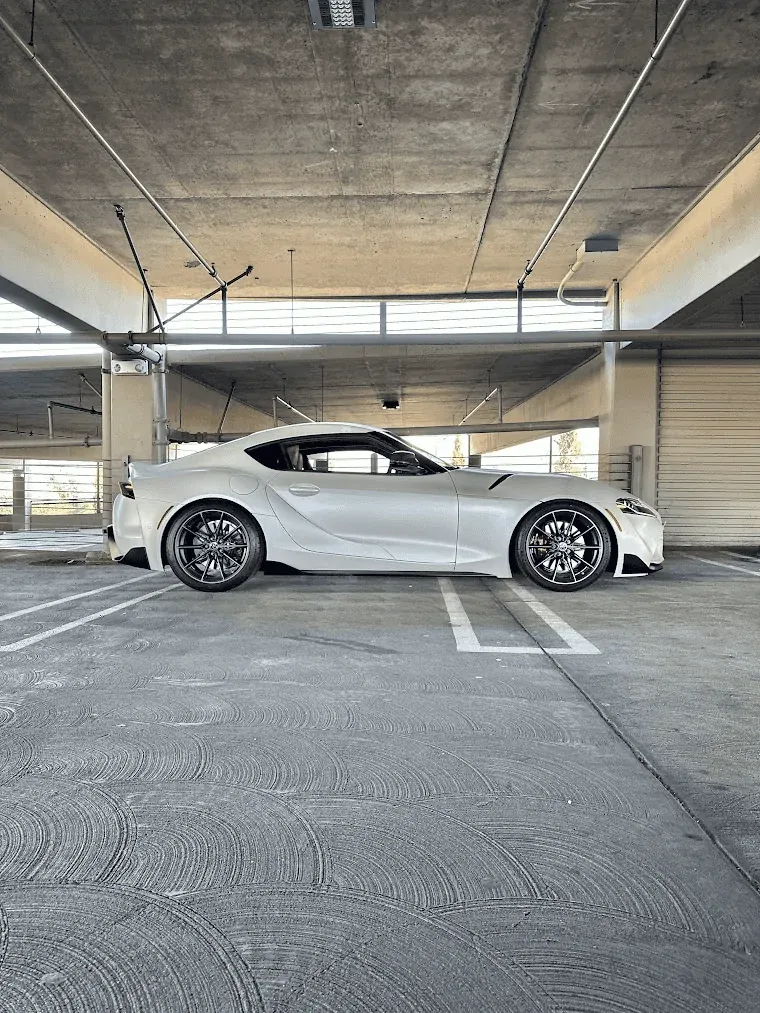 A white GR Supra in profile on a concrete parking deck