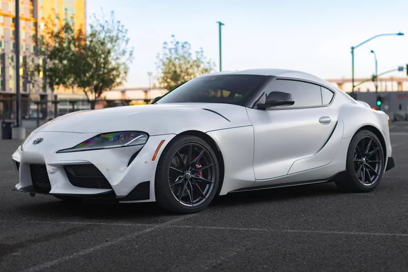 A white GR Supra parked on an empty lot in evening light, front three-quarter view